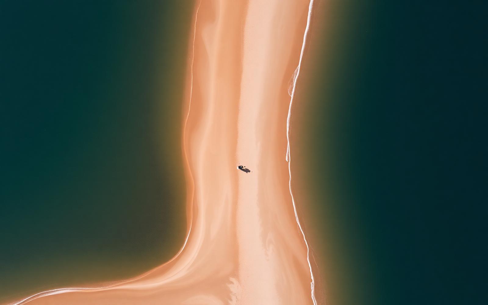 Aerial view of a lone figure walking along a sandbar between deep water